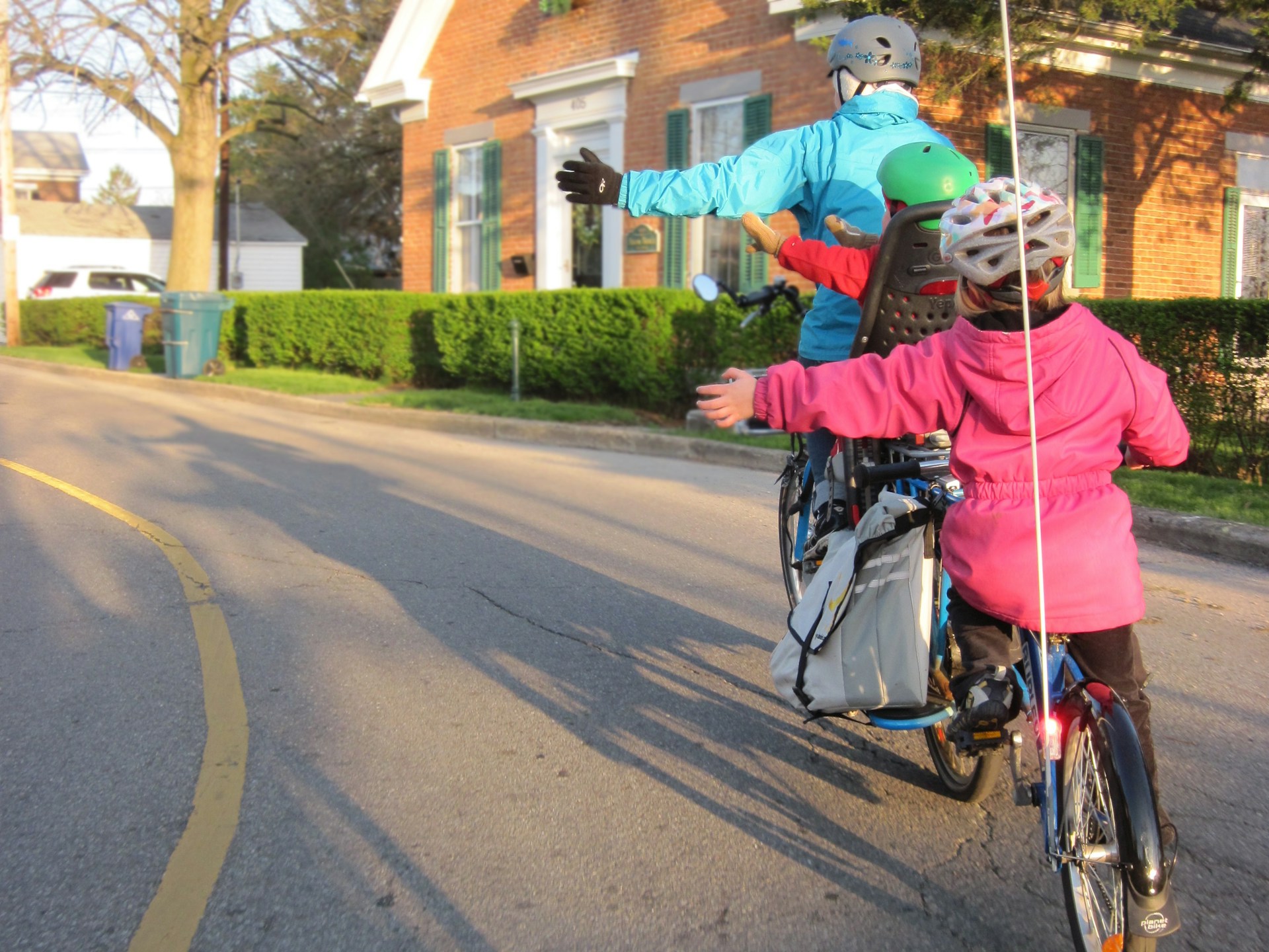 Two children are shown from the back biking with a parent and signaling a left turn.