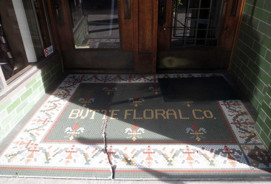 Butte Floral Co, gold tile letters on green background, floral patterned border in red, green, white and gold