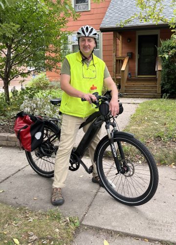 A man poses on a sidewalk with his e-bike.