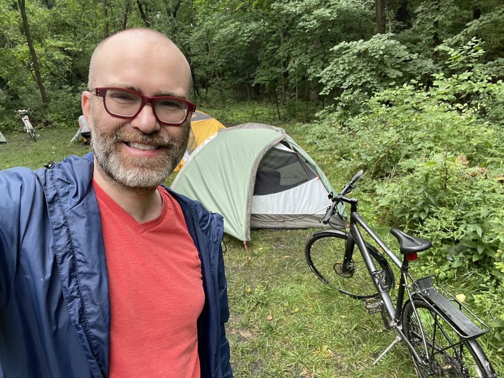 A man outdoors in front of a tent and a bicycl;e