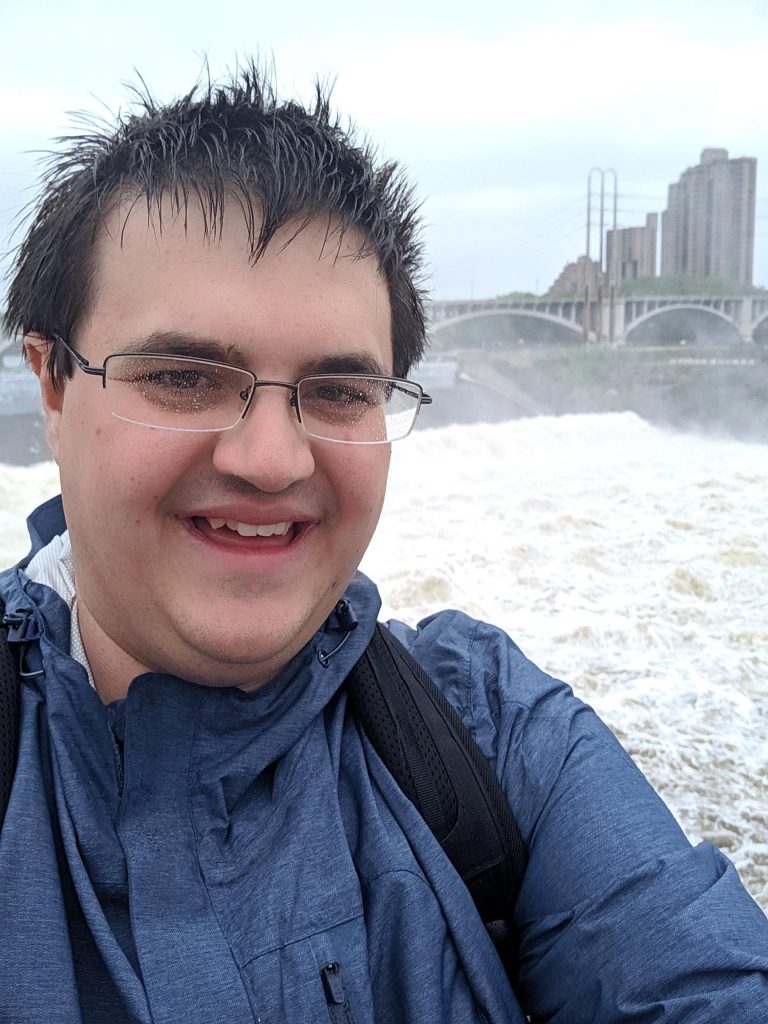 A man with wet hair stands in front of a waterfall near downtown Minneapolis.