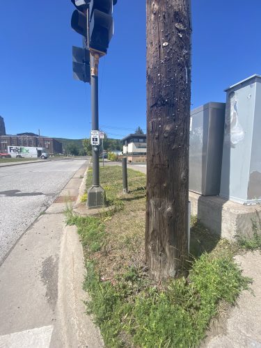 Another view of a pedestrian call button on a traffic light pole that's set back from the sidewalk, with another utility pole blocking access.