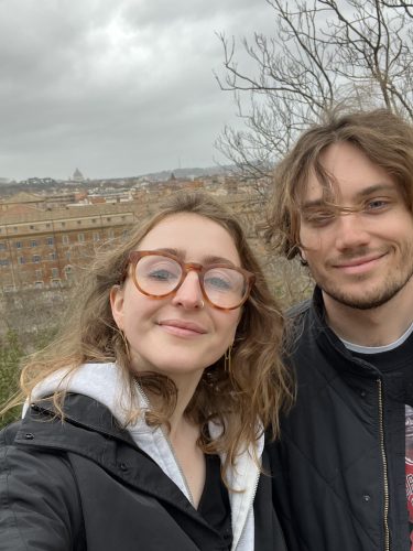 A woman and man pose in front of an open field.