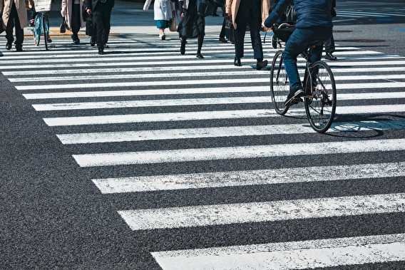 A painted crosswalk, with a view of people's walking feet and one bicyclist.