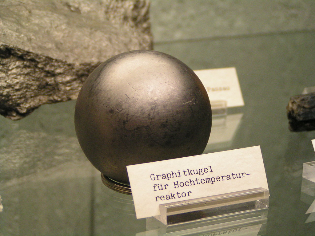 Museum display of a graphite sphere used in a high-temperature nuclear reactor, shown on a display stand with a German descriptive label.