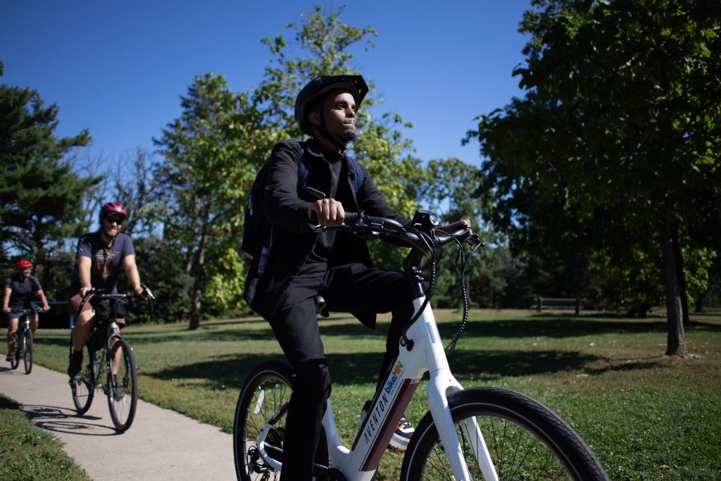 Three men ride e-bikes outdoors on a sunny September day.