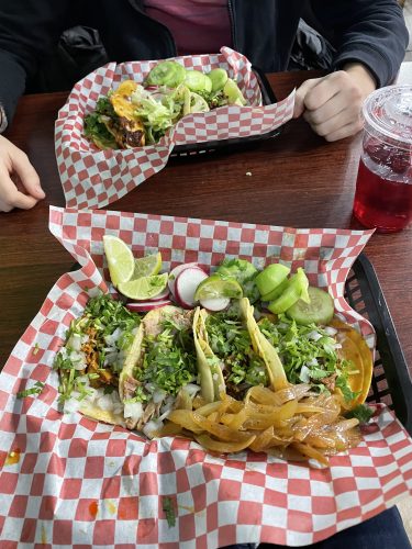 Tacos in a plastic lined tray shown atop a table at Taqueria y Birrieria las Cuatro Milpas.