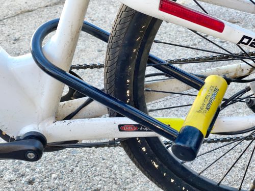 A white bike with a yellow and black U-lock through its frame.