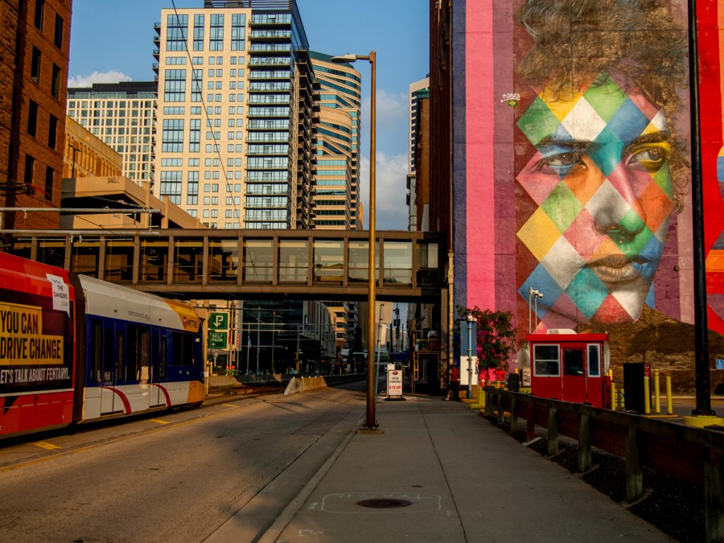 A light rail train in downtown Minneapolis, with a mural depicting Bob Dylan on the right.