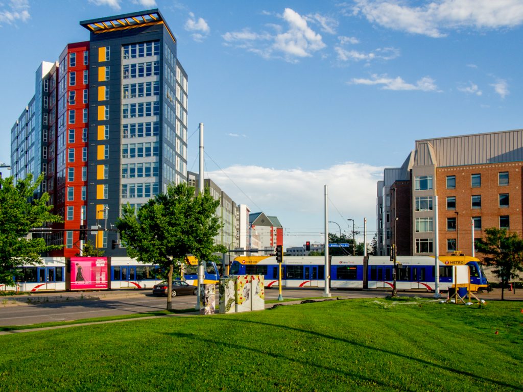 A train crossing University Avenue, with the colorful WaHu apartments in the background.