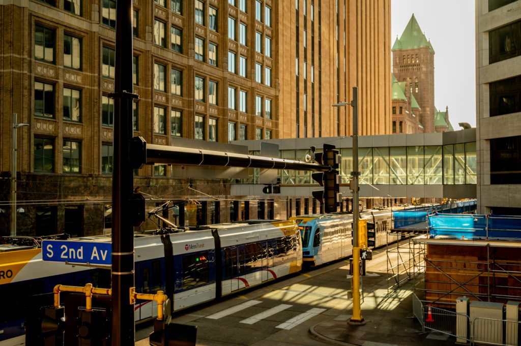 A train passing under a skyway in downtown Minneapolis, with City Hall in the background.