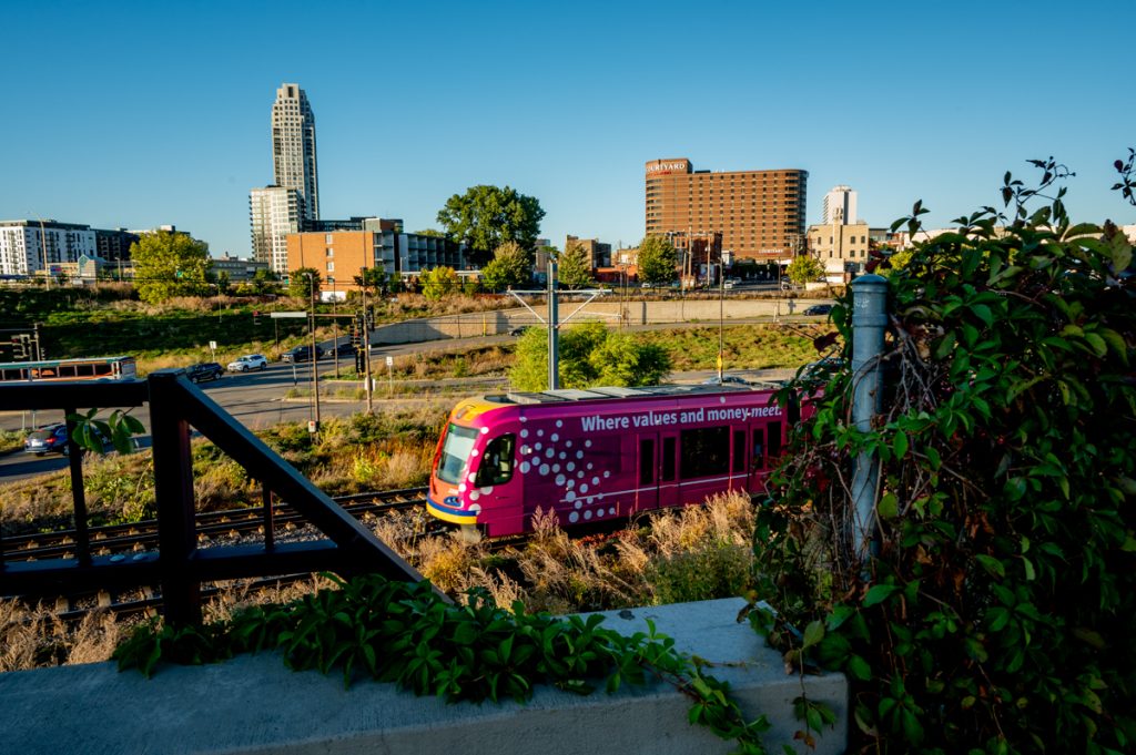 Foliage in the foreground frames a train leaving downtown, with the Courtyard by Marriott in the background.