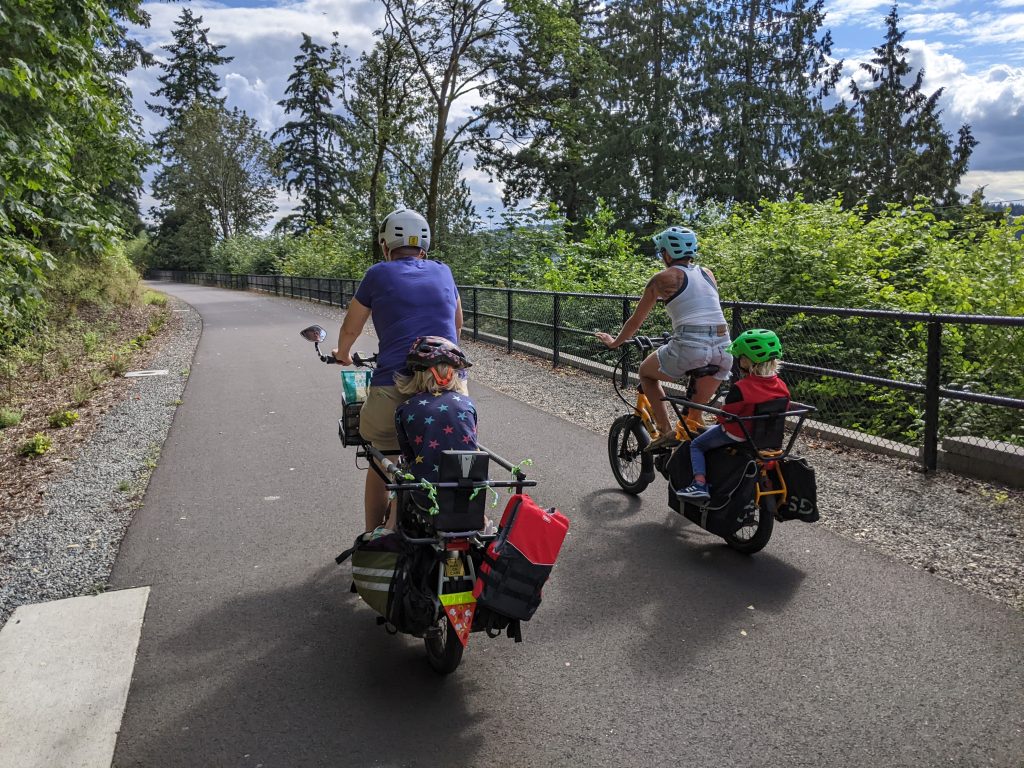 Two adults riding family e-bikes with children in the back seats.