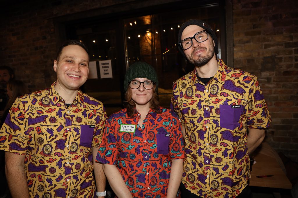 A woman flanked by two men pose in matching shirts at Lake Monster Brewing in St. Paul.
