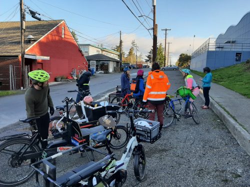 A group of cyclists stopped for a break on a shaded street.