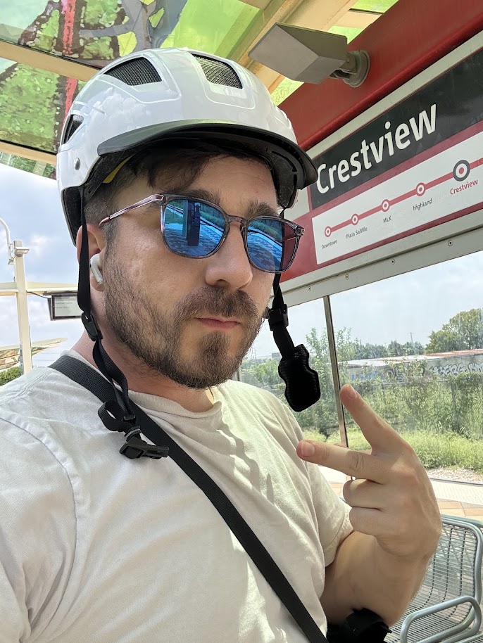 A man holds up two fingers wearing a helmet from the inside of a light-rail train.
