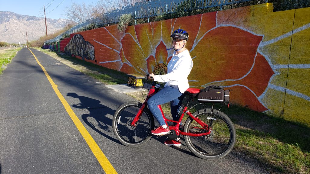 A cyclist posing on a paved bike trail with brown mountains in the background.