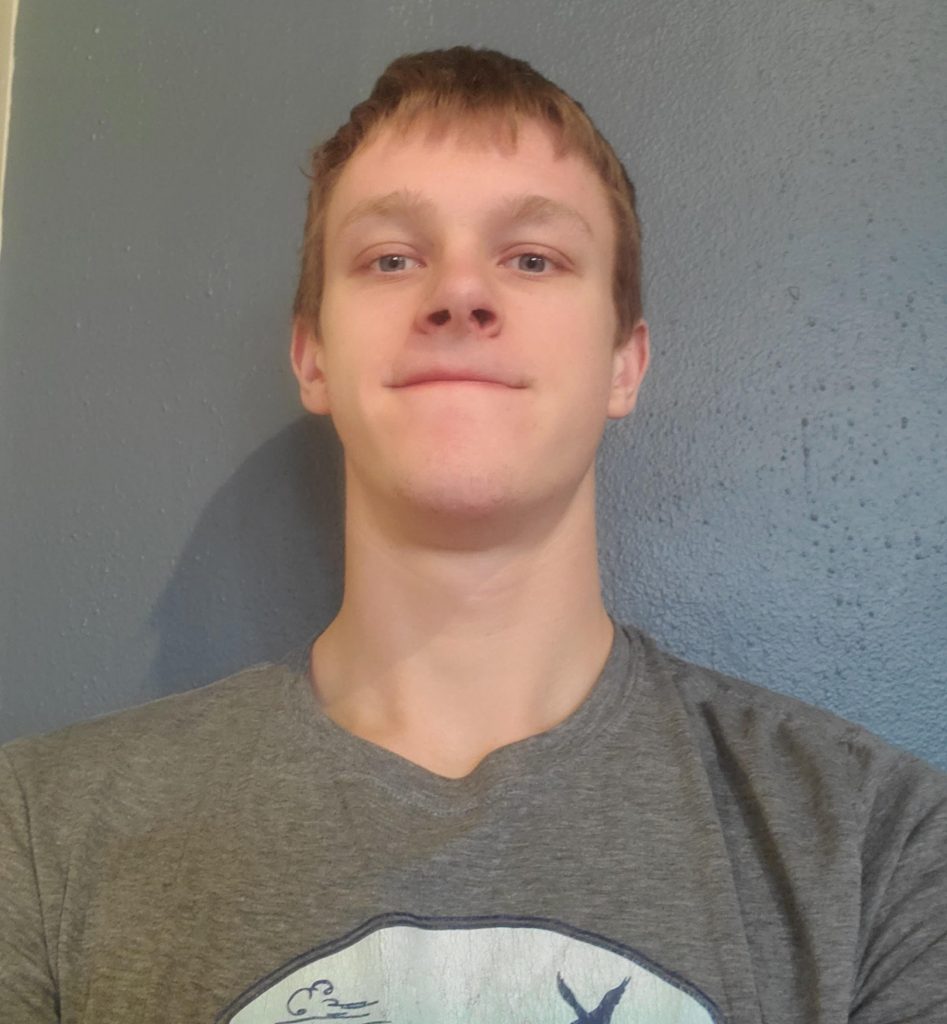 A man looks at the camera, against the wall.