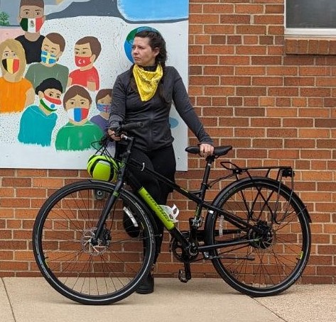 A woman poses with her e-bike in front of a mural and a brick wall.