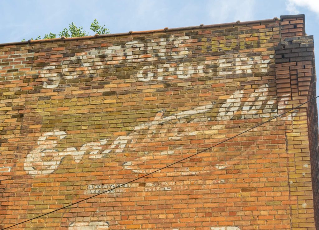 Closer view of fading Schoen's Grocery sign painted on brick building. 