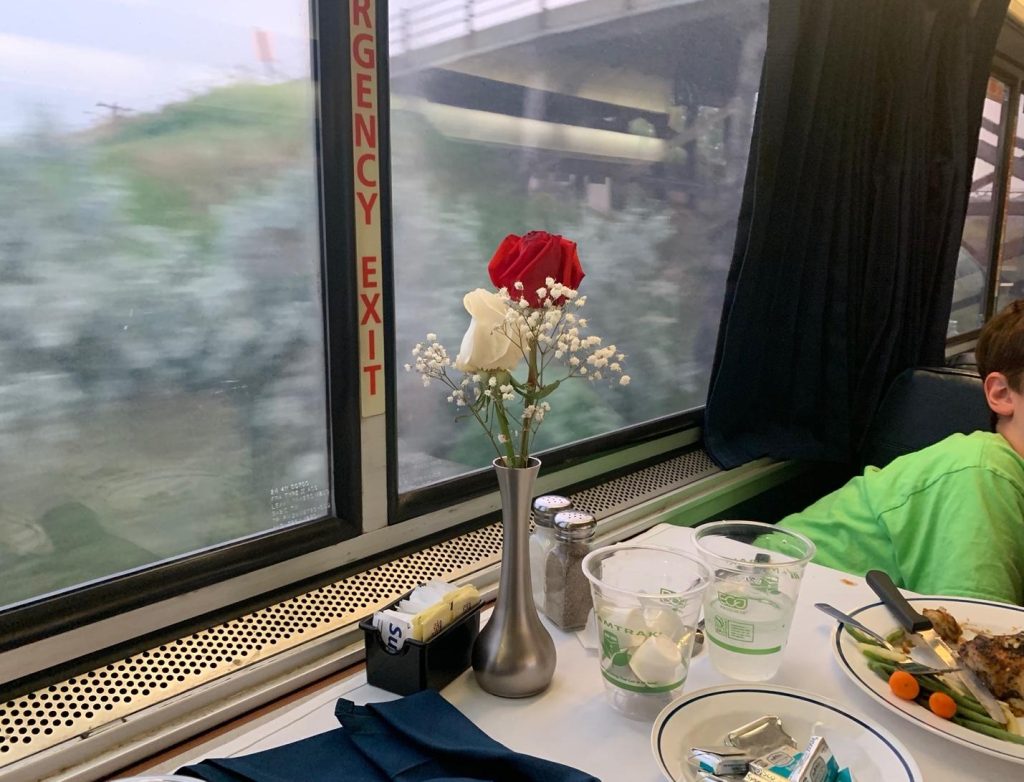 A table in an Amtrak dining car, with a vase of flowers and plates on it