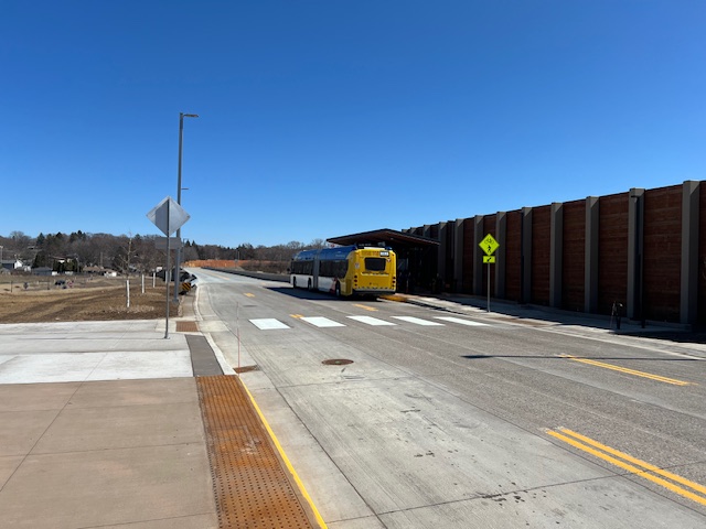 Looking east from the Etna Station platform, a METRO Gold Line bus is stopped under a covered shelter.