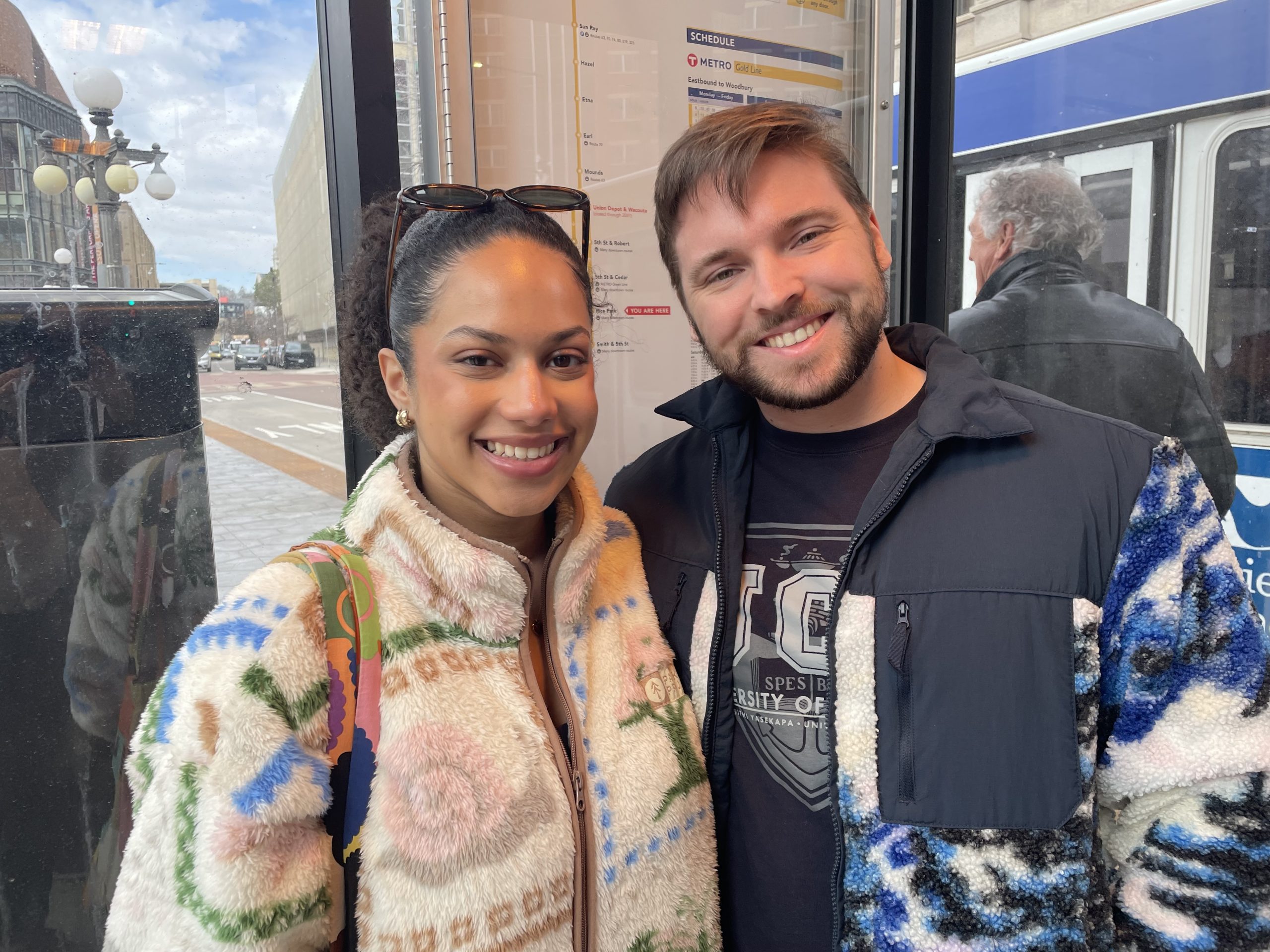 A woman and man, both smiling, post for a photo at a bus stop in downtown St. Paul.