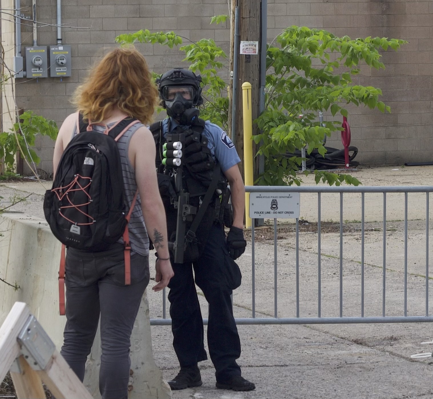 A red-haired woman with a backpack faces a police officer who has a helmet on.