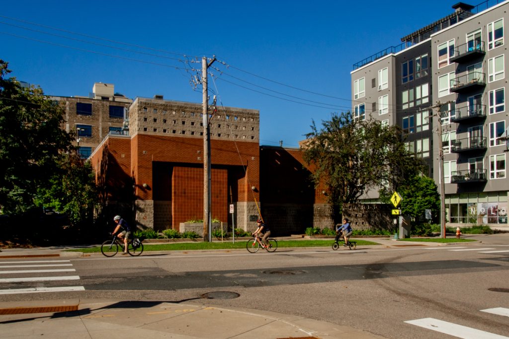Three cyclists ride down a bike path on a city street with buildings in the background.