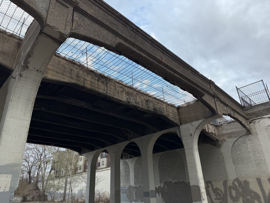 Looking up at the 10th Avenue bridge showing a metal mesh covered hole in the western deck. The sky is visible through the hole in the bridge.