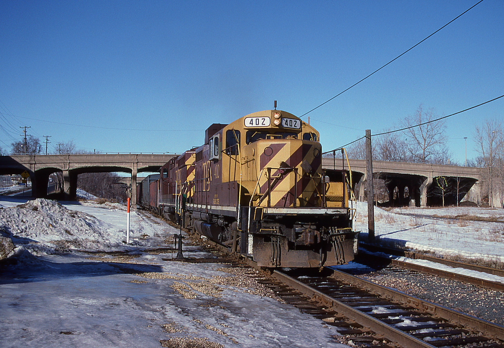 TC&W locomotive 402 pulls a train heading east in the winter. The old 4th Avenue bridge with ten spans is behind.