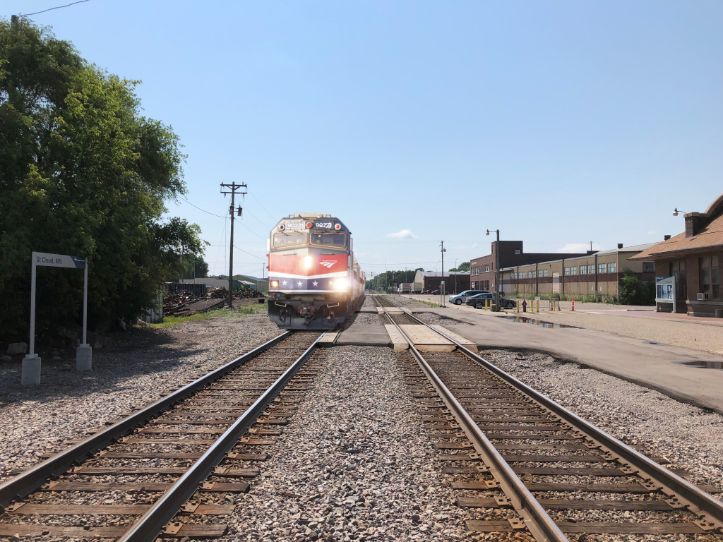 An Amtrak train with a red, white, and blue locomotive approaches the St. Cloud, MN.