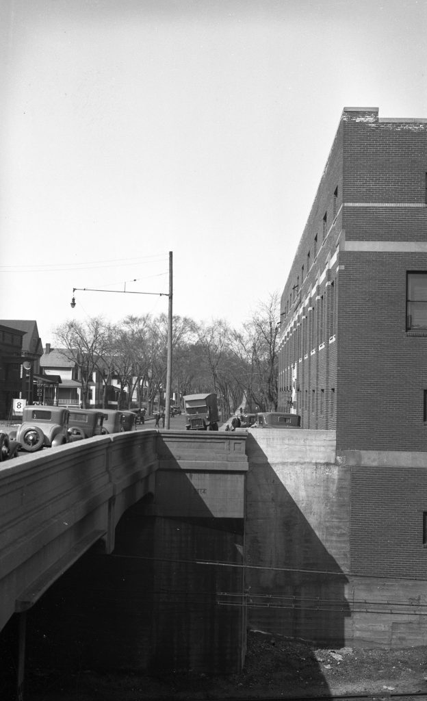 Looking North up 3rd Avenue from across the trench. A three story and basement brick building stands to the east of the avenue and forming a wall in the trench.
