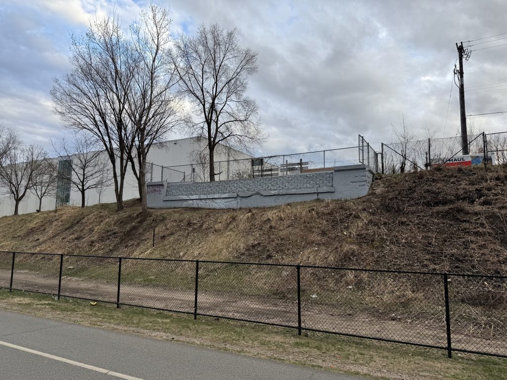Smaller Clinton Avenue S bridge abutment sits to the South of the Midtown Greenway. It is painted blue and has wall pavers filling in the void where the bridge would rest on.