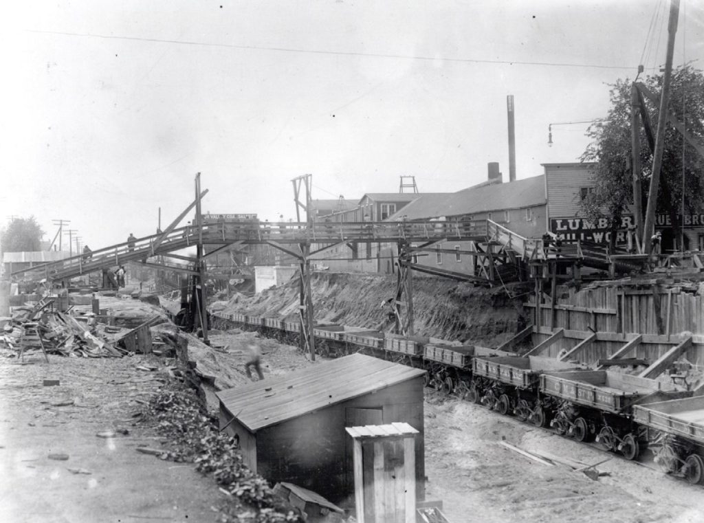A temporary wooden footbridge over the trench and a line of empty work cards for hauling out earth.