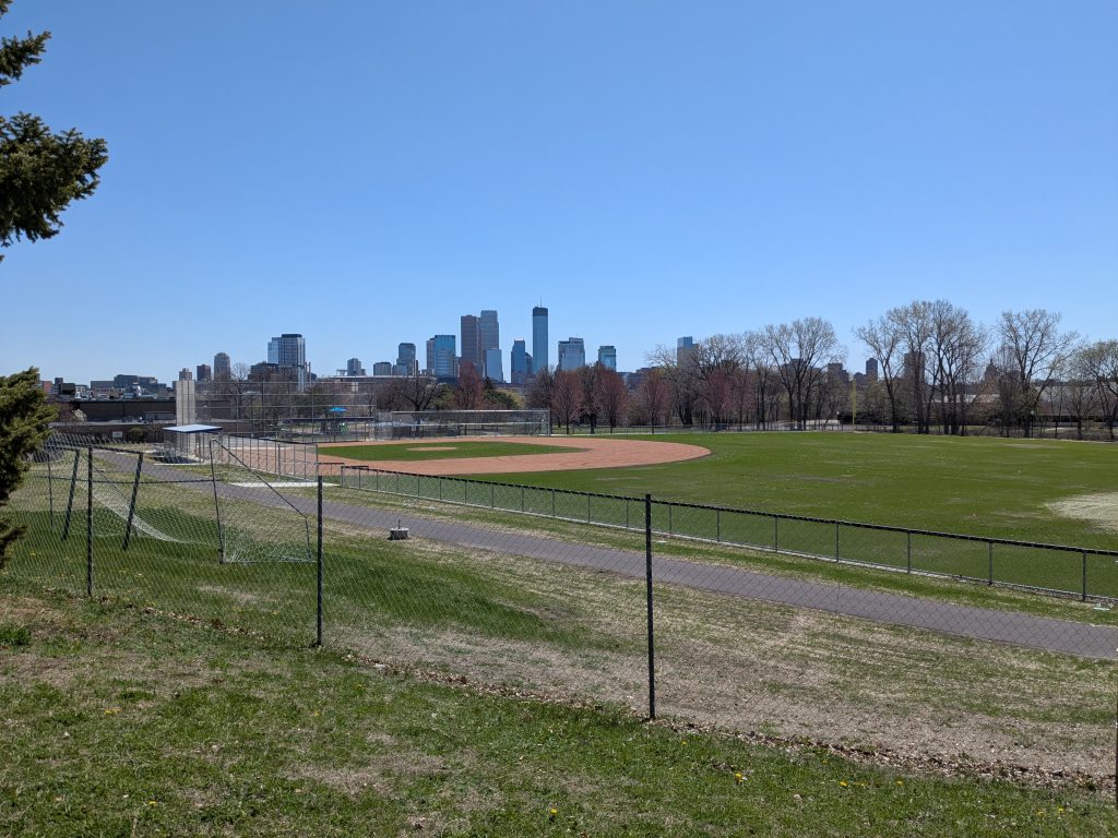 a diamond playing field with the downtown Minneapolis skyline in the background