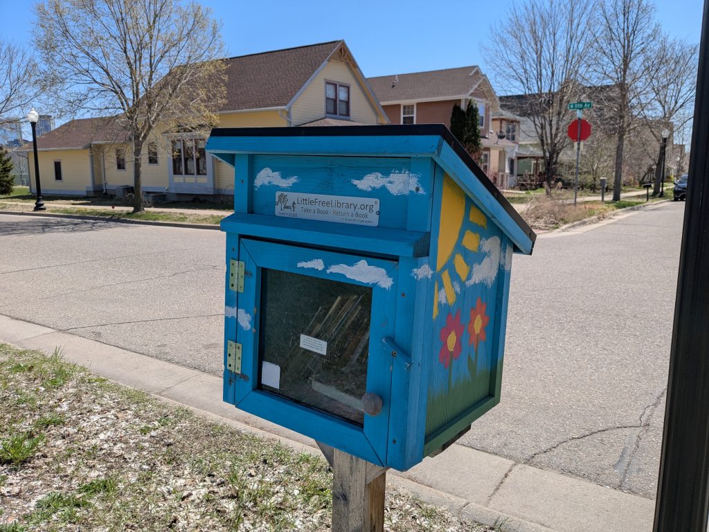 blue little free library painted with sun, clouds, flowers, grass