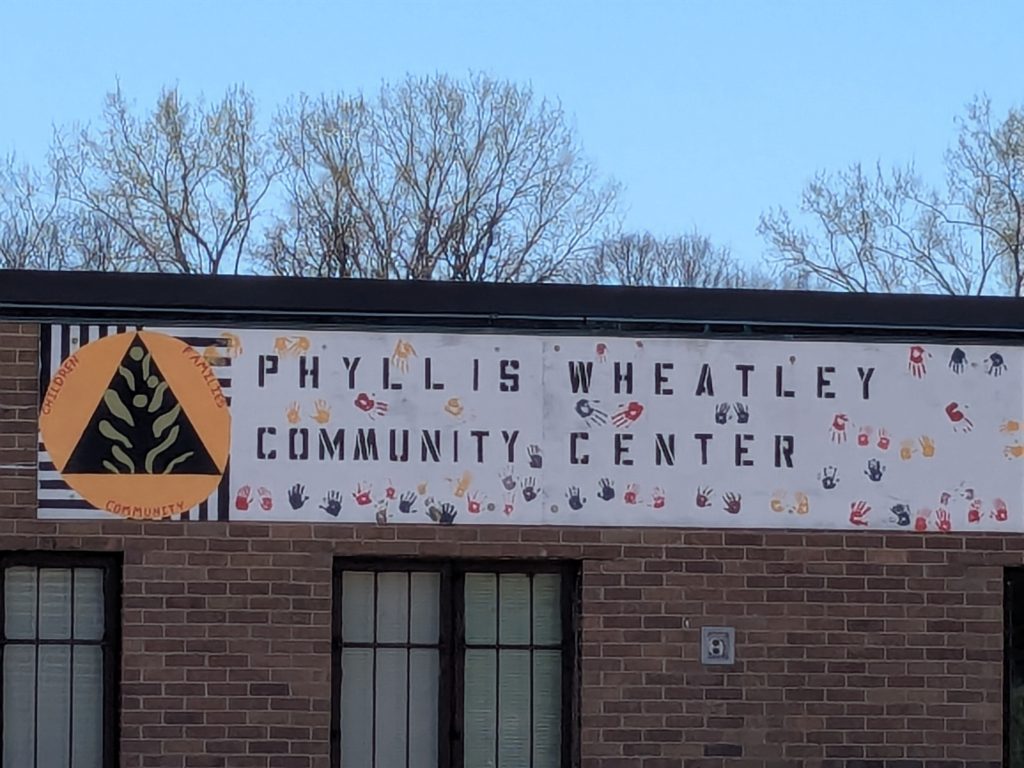 sign on brick building with name Phyllis Wheatley Community Center, logo with three components children, families, and community, and handprints