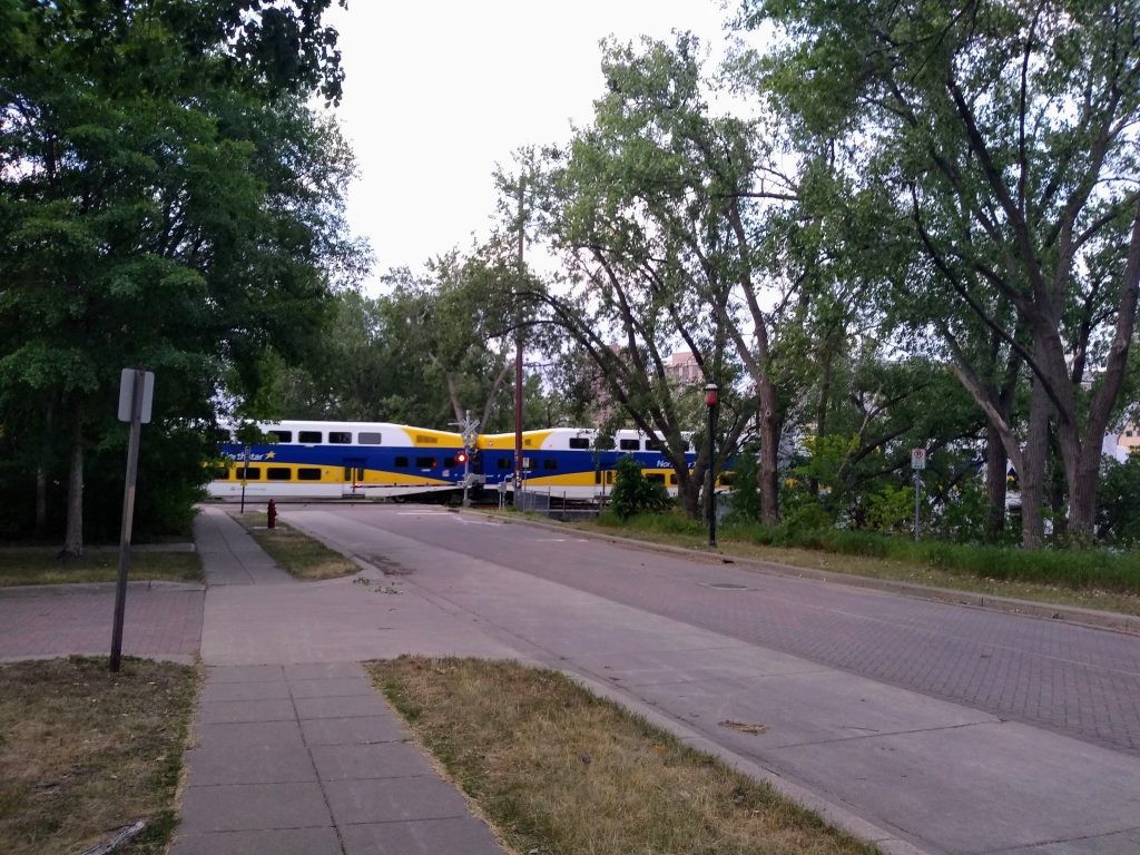 commuter rail with white, blue, and yellow livery crossing street