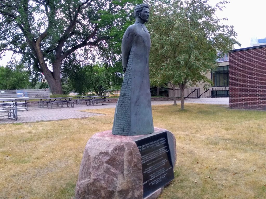 sculpted statue of figure in frock with inscriptions on stone pedestal with inscribed plaque