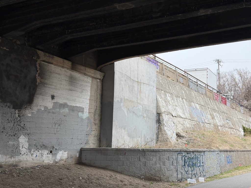 Northeast wing wall with new concrete in front at the Pleasant Avenue S bridge. The concrete retaining wall continues to the east.