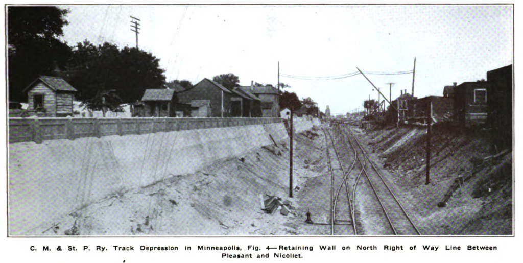 Two main tracks in the trench with a retaining wall on the north side spanning multiple blocks between Pleasant and Nicollet avenues.