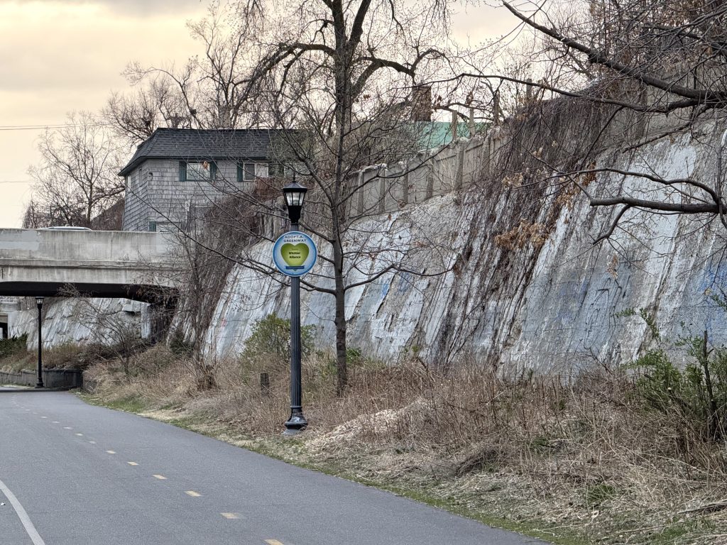 Looking at the concrete retaining wall to the North of the corridor with some deterioration with the Pillsbury Avenue S bridge in view.