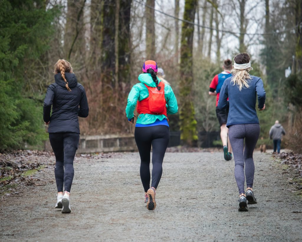 Three women photographed from the back running up a slight incline in the woods on a race.