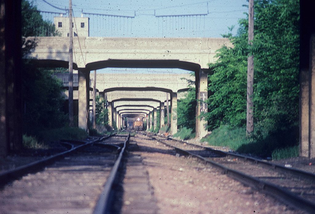 1990s era photo. TC&W 406 approaching on the right track while looking down the tracks just above the ground. Tell0tails are hangings.