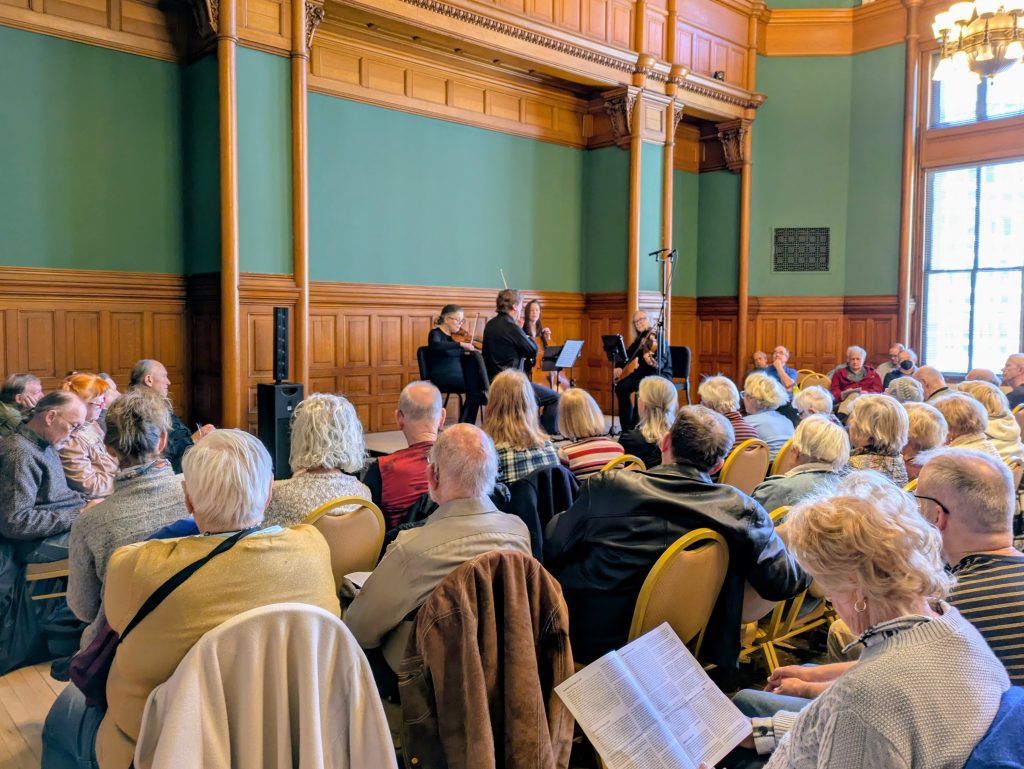 A room full of people enjoy listening to a string quartet in Landmark Center.