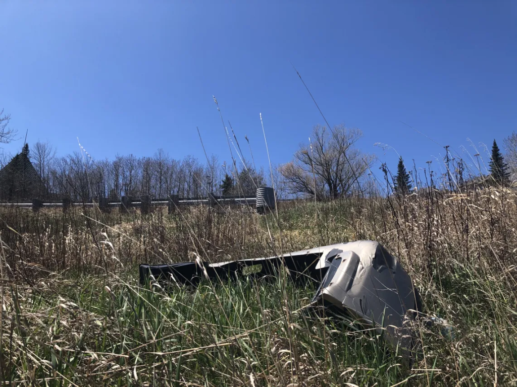 A damaged car bumper lying in a field near an intersection.