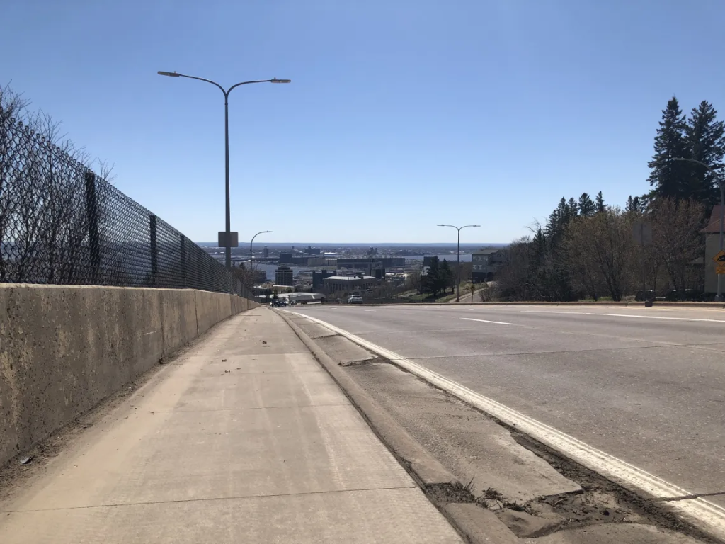 A view toward Saint Louis Bay from Mesaba Avenue in Duluth, Minnesota, with grain silos and industrial buildings visible down a long hill.
