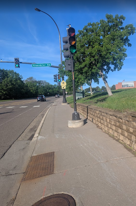 Sidewalk with traffic signal posts set in concrete blocking part of the sidewalk in front of Hopkins North Middle School. 