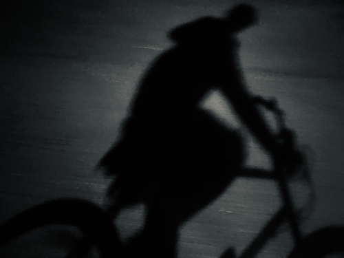A silhouette of a woman riding a bike at night.